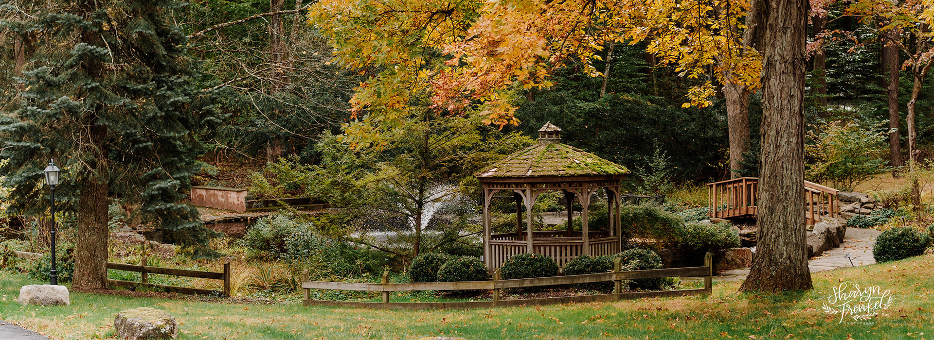 Gazebo and walking trail with bridge, surrounded by autumn trees and foliage