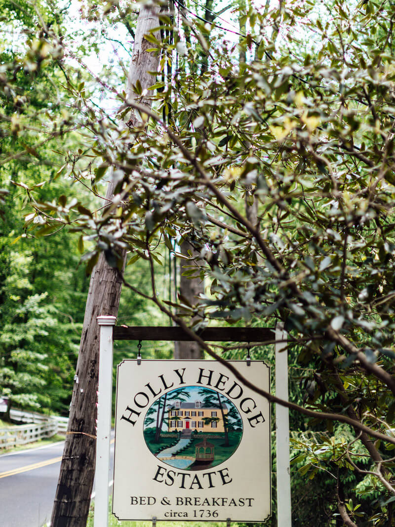 Outdoor sign with "Holly Hedge Estate" and a drawing of The Inn, surrounded by rhododendrons and trees