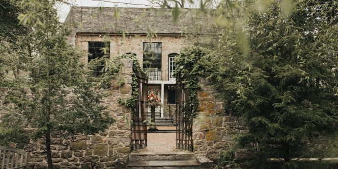 View of an old stone building, partially hidden behind a stone wall and green tees.